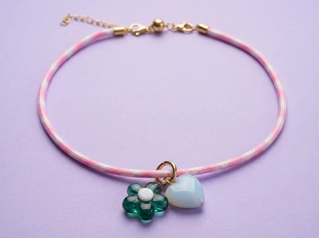 Necklace with floral charm and heart-shaped pendant on a pink cord against a purple background