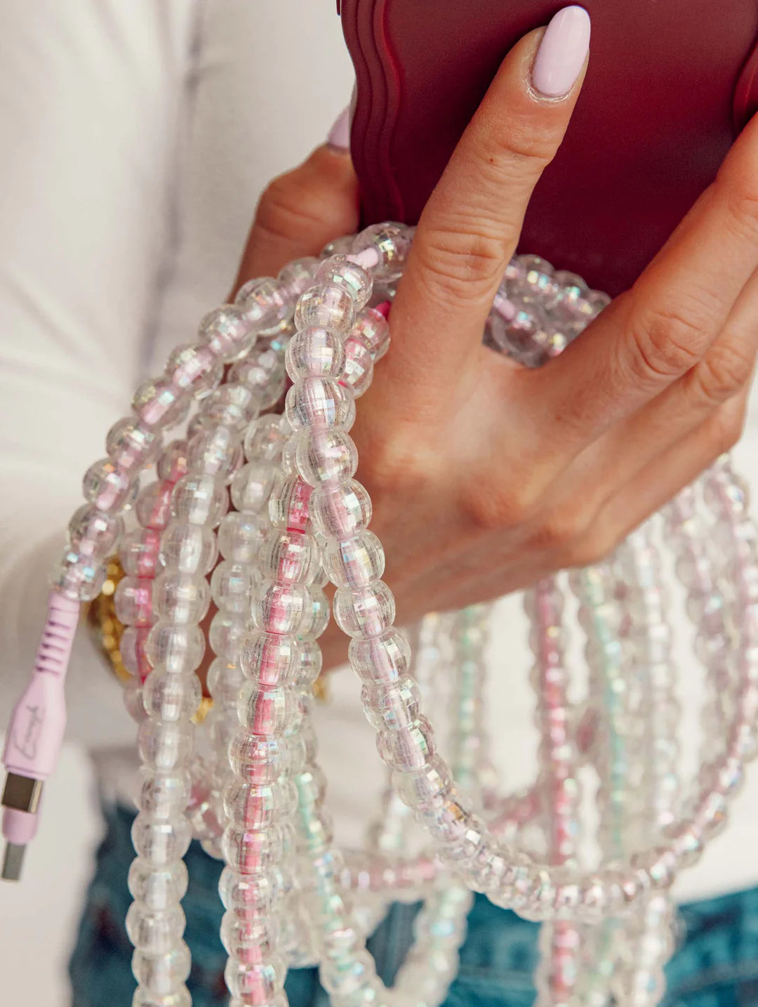 Close-up of a hand holding a pink electronic device with beaded cables.