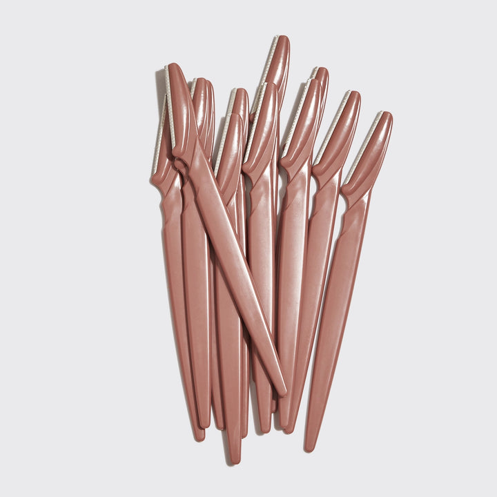 Set of rose gold eyebrow razors on a light gray background