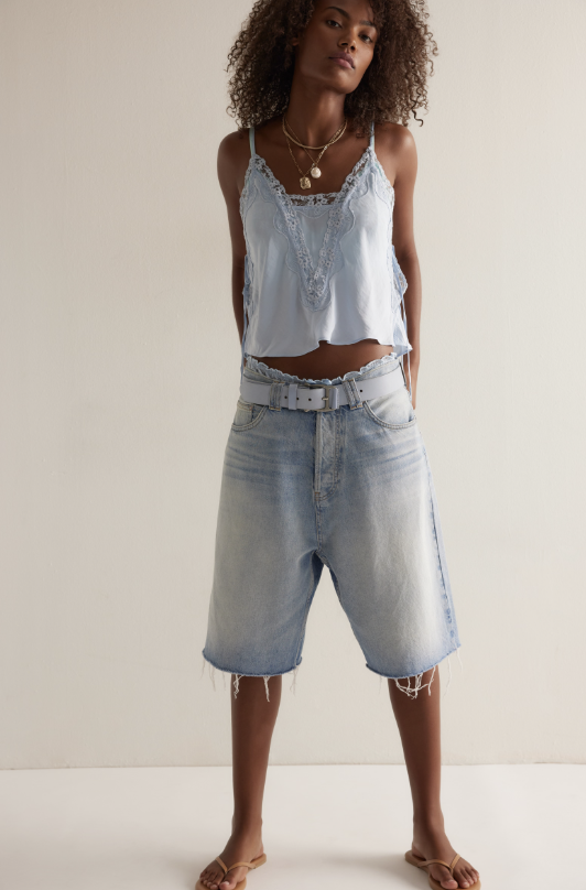Woman wearing a light blue lace top and denim shorts on a white background