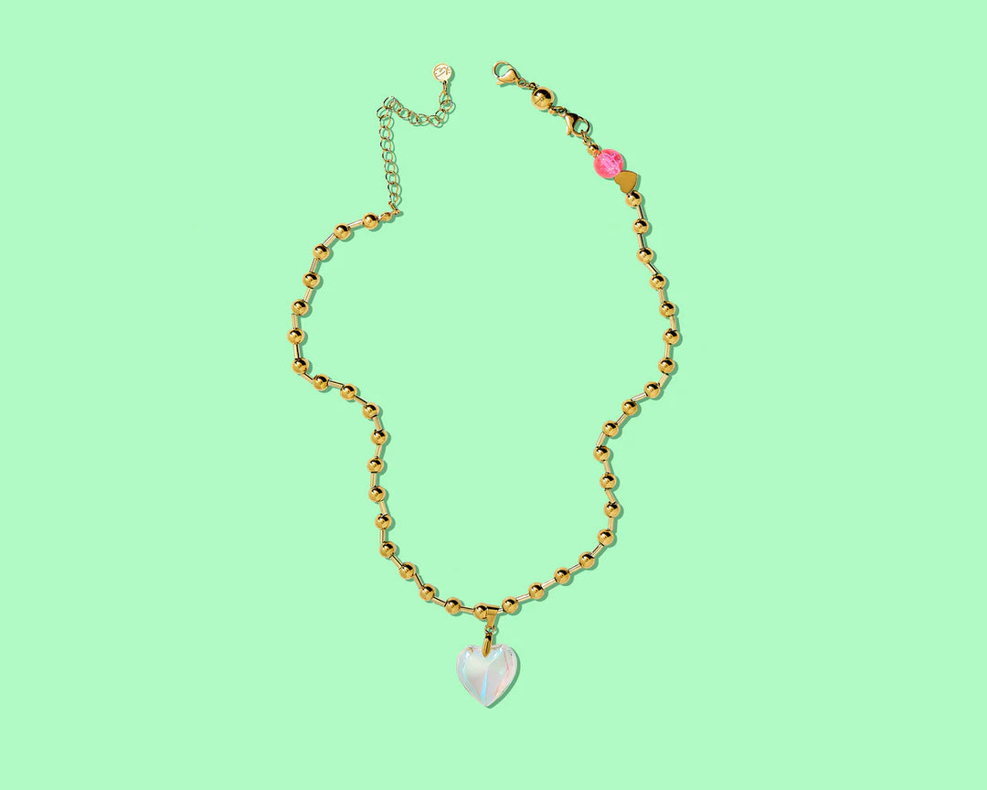 Gold necklace with a heart-shaped pendant on a light green background