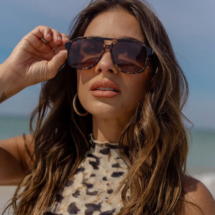 Woman wearing sunglasses with a leopard print top on a beach
