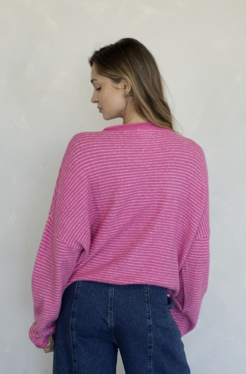 Woman shown from behind wearing pink stripe cardigan and jeans on plain background