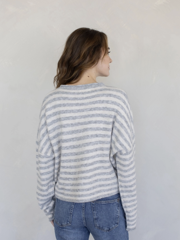 Woman wearing grey and white stripe cardigan and blue jeans on plain background