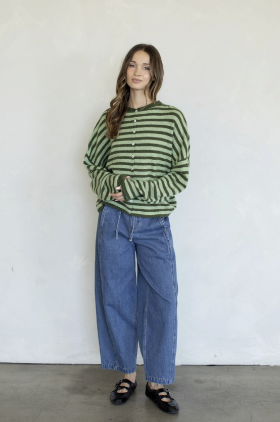 Woman wearing green stripe cardigan and blue jeans on plain background