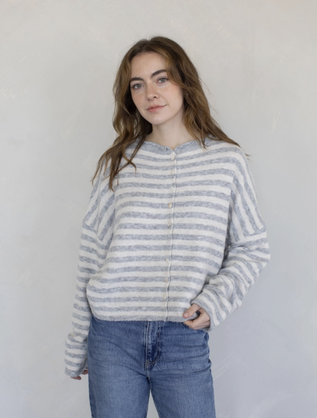 Woman wearing grey and white stripe sweater and blue jeans on plain background