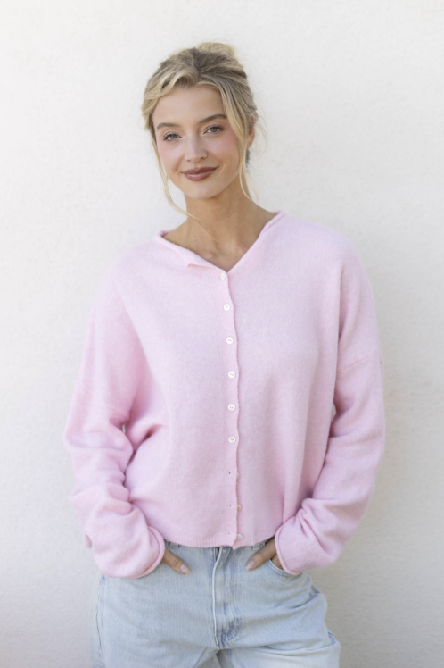 Woman wearing light pink cardigan and jeans on plain background