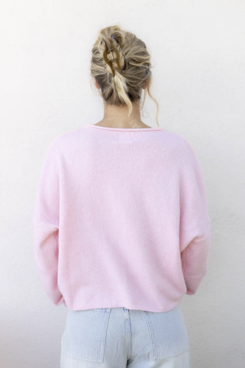 Woman shown from behind wearing light pink cardigan and jeans on plain background