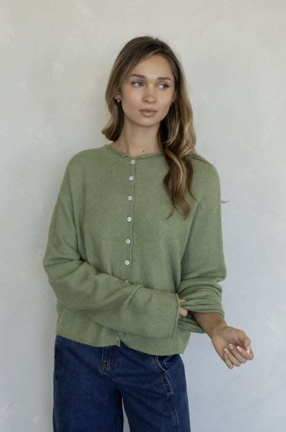 Woman wearing sage green cardigan and jeans on plain background