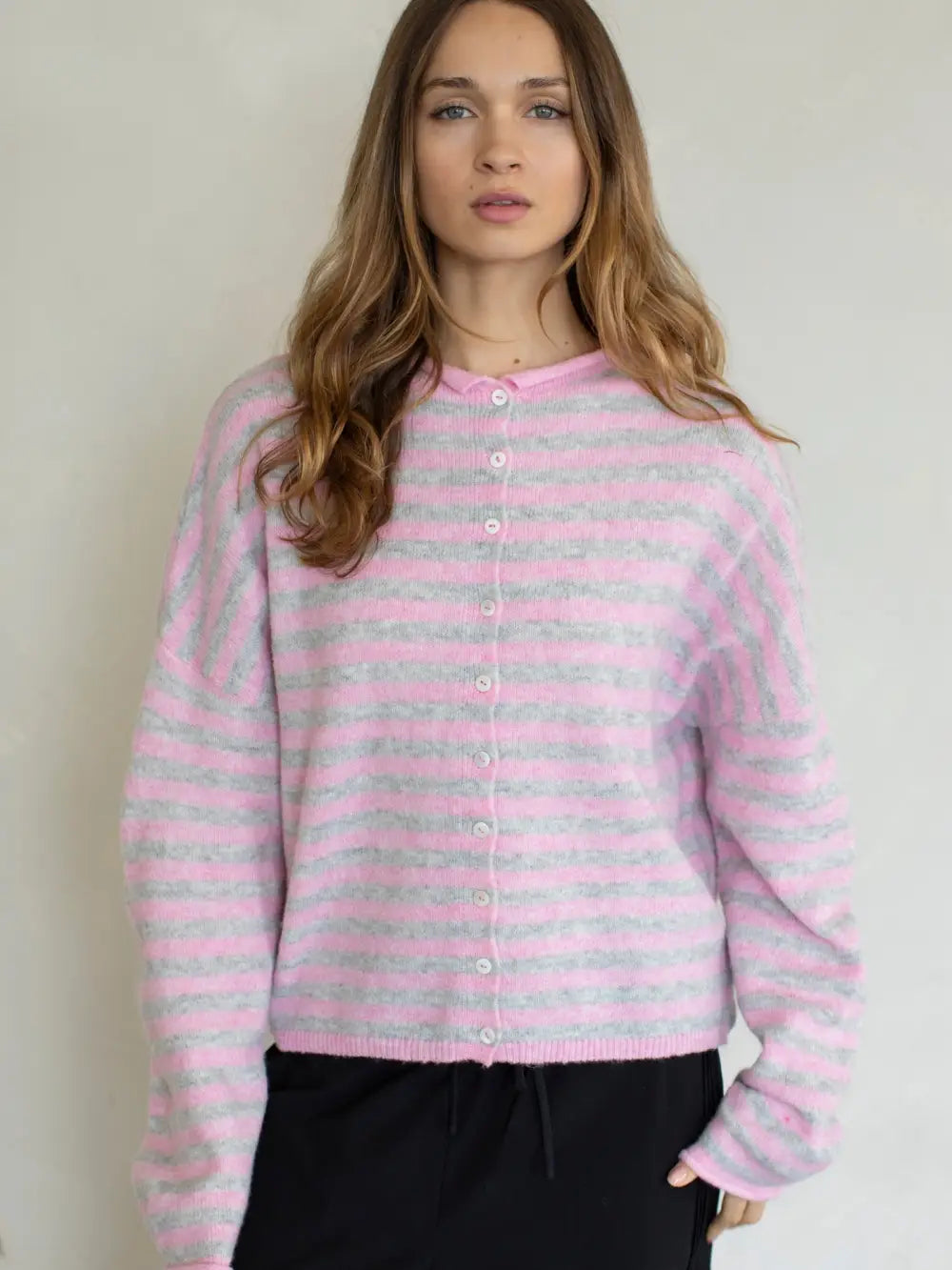 Woman wearing a pink and gray striped cardigan against a plain background