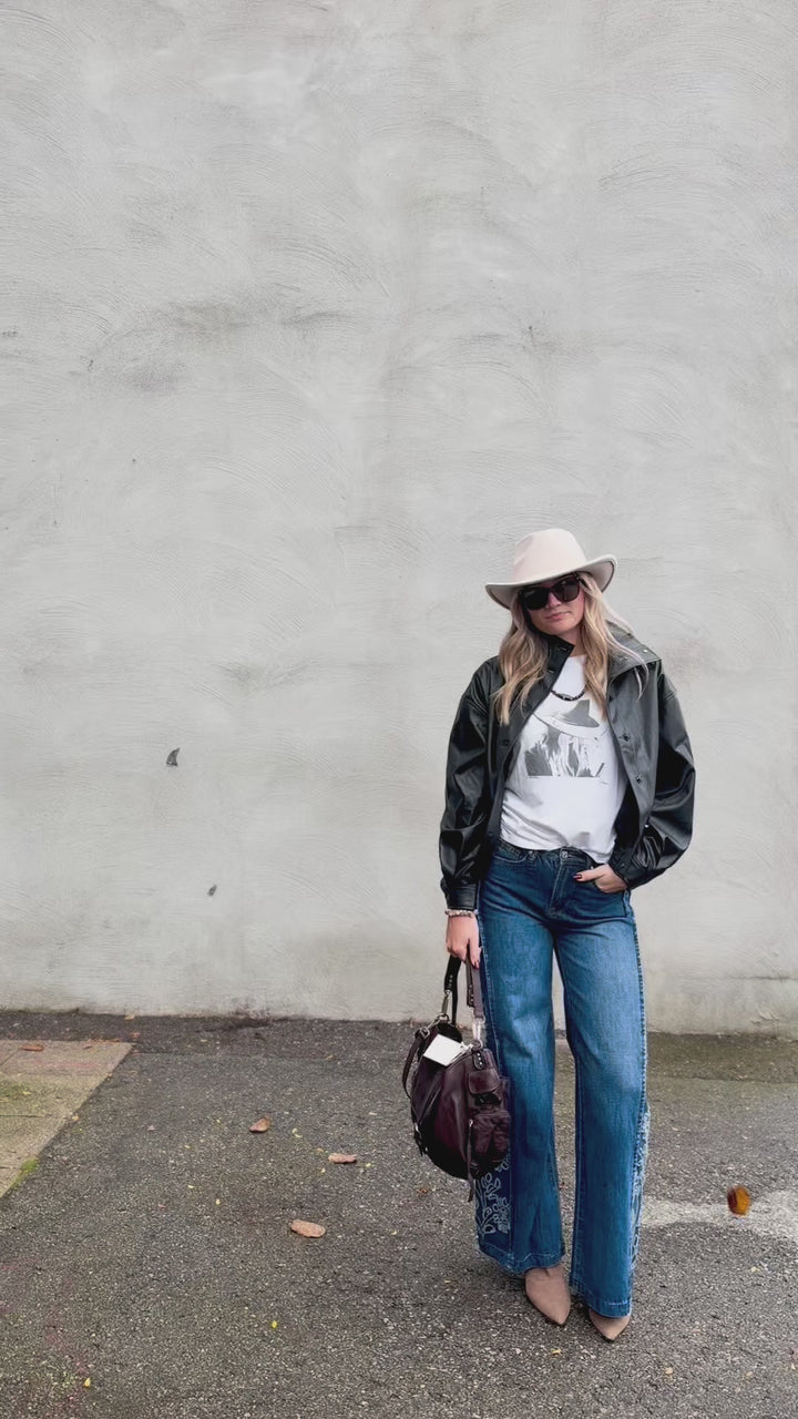 Woman wearing medium wash denim jeans with floral cutouts on sides paired with graphic tee and leather jacket standing outdoors