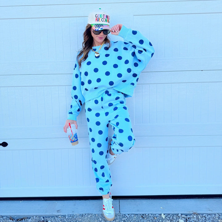 Person wearing a blue polka dot outfit with a colorful hat against a light blue wall.