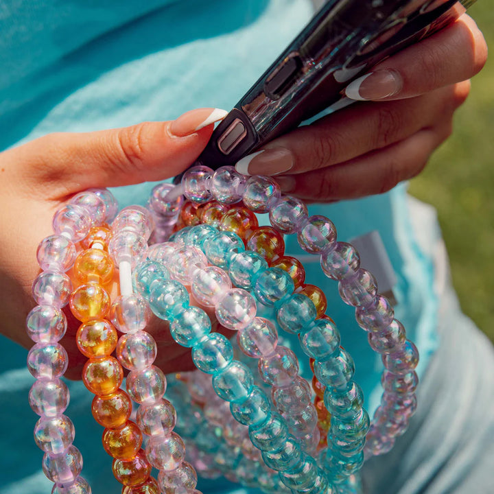 Colorful beaded bracelets held by a person with a phone in a natural setting