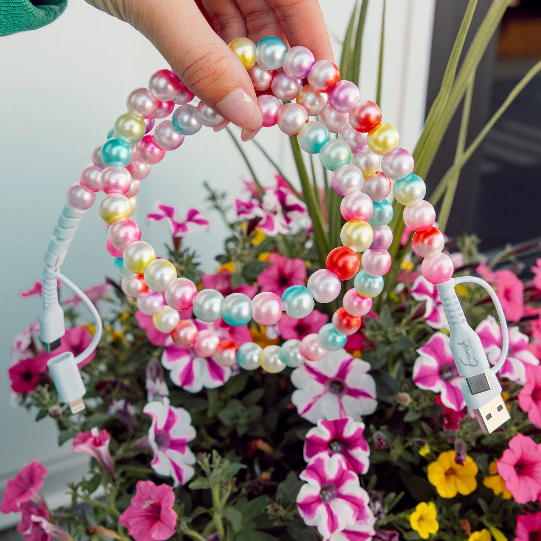 Colorful beaded cable shaped like a heart held by a hand with flowers in the background