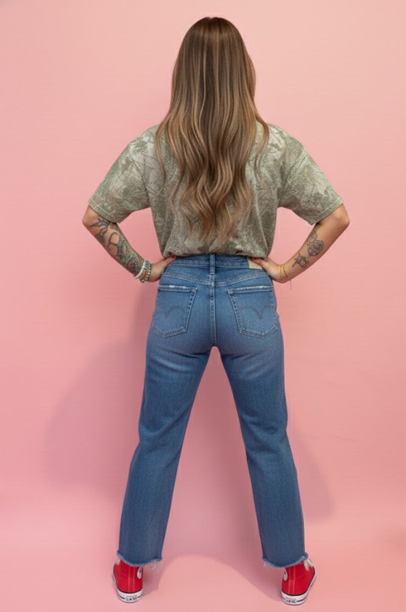 woman standing in front of pink wall wearing camo tshirt and jeans.