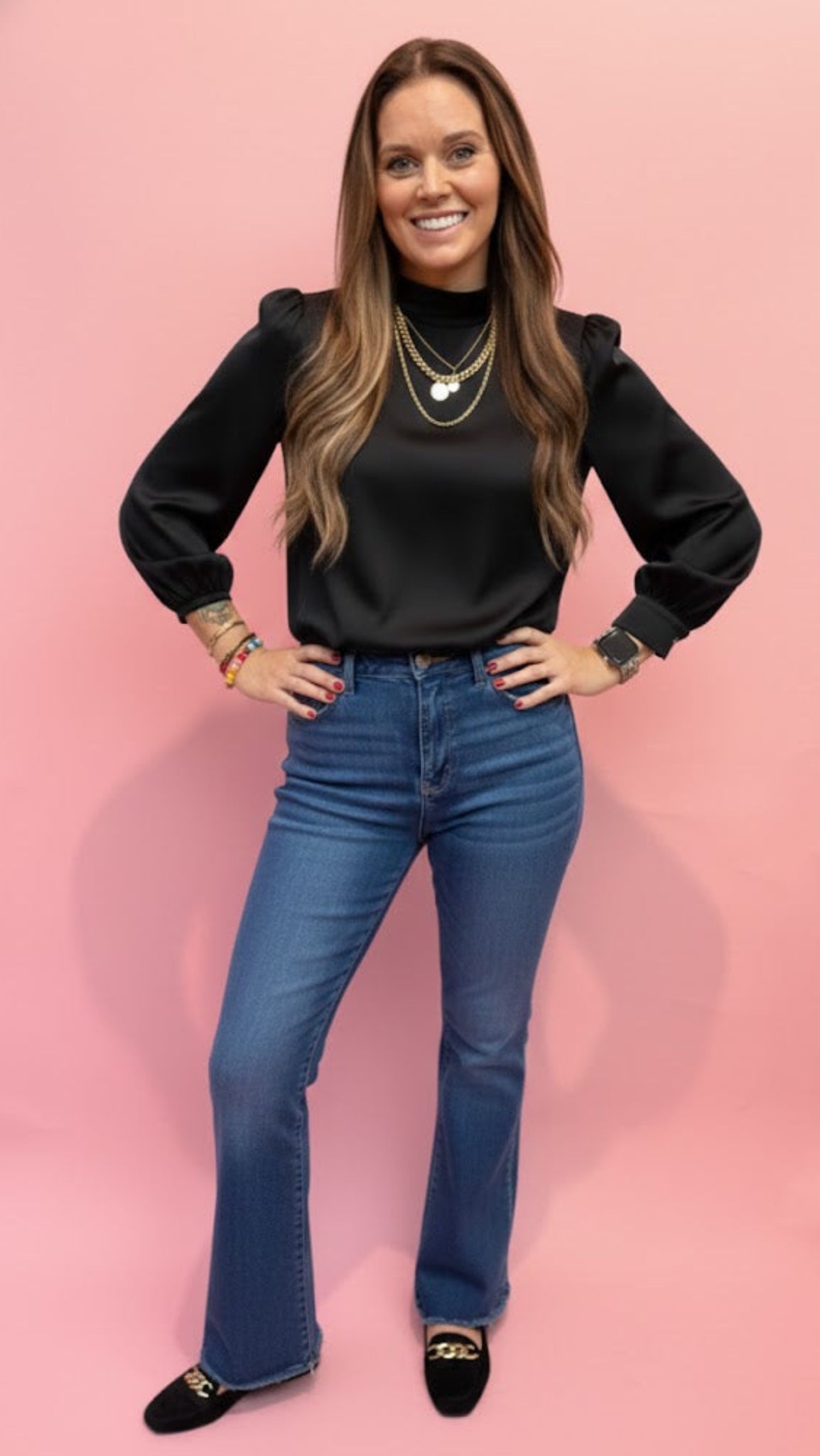 woman wearing high neck satin black top with jeans in front of pink wall