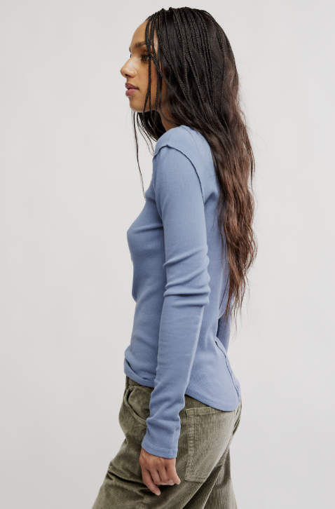 Woman wearing a light blue long-sleeve top and green pants against a white background