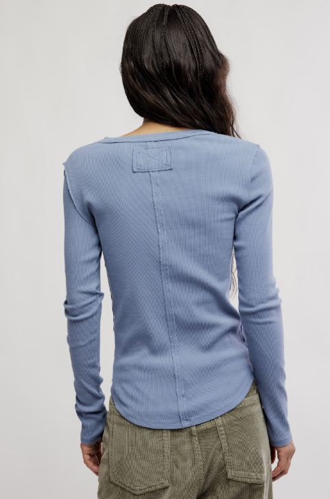 Person wearing a blue textured long-sleeve top and beige pants on a plain background