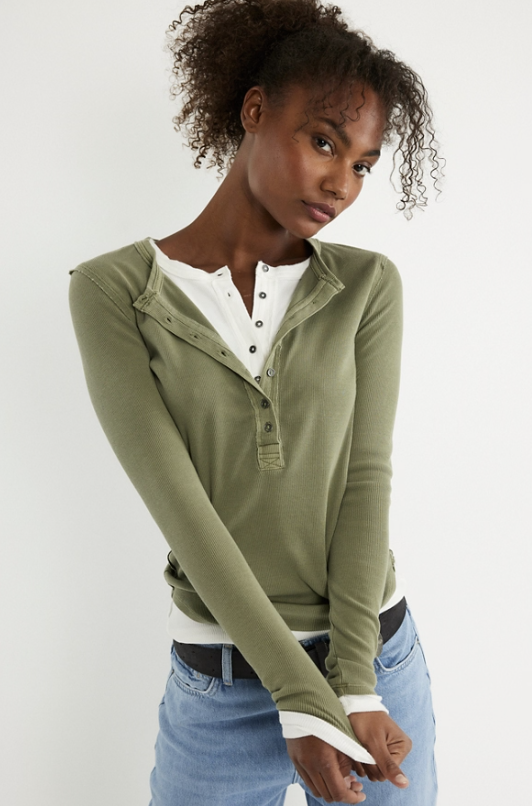 Woman wearing a green long-sleeve shirt over a white top with blue jeans on a white background